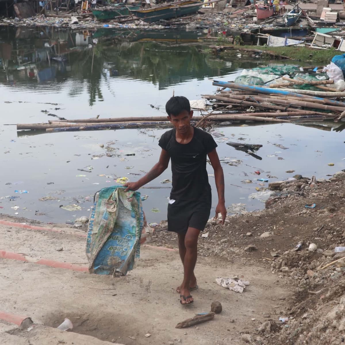 Marlo walks past a former tahungan site in Little Samar Shore, Navotas City, now buried under rocks and dumped earth that have erased much of the mussel-growing area once used by local fisherfolk. (Photo by: Zaijan Rio Tengson)